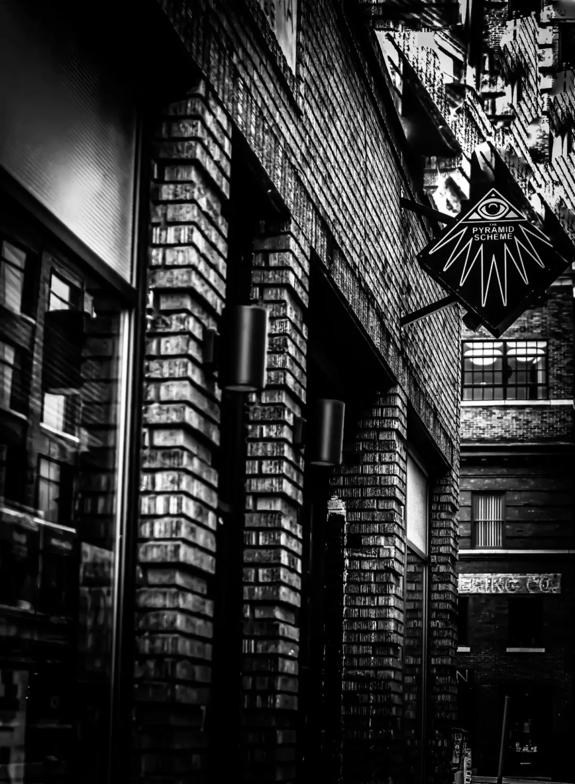 The exterior of the Pyramid Scheme bar. Brick building with black diamond sign with logo.