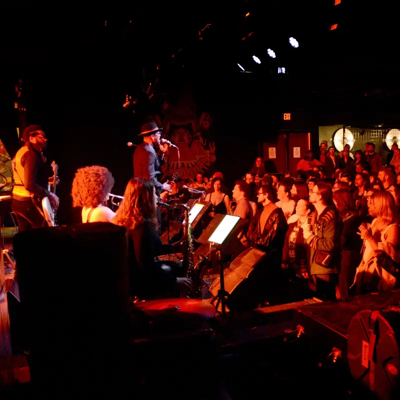 Artist performing on stage at The Pyramid Scheme in front of a large crowd and red lights.