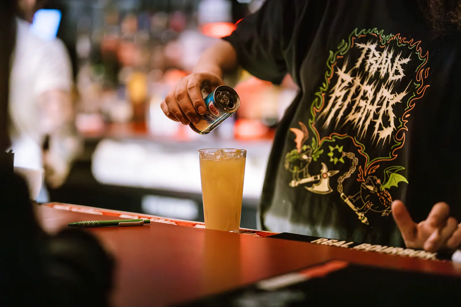 bartender pouring pineapple juice can into mixed drink glass