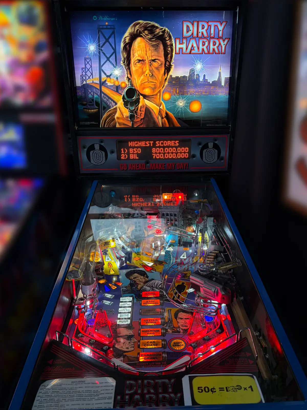 A brightly lit "Dirty Harry" pinball machine. The backbox shows Clint Eastwood with a focused expression, holding a gun over the San Francisco skyline. The game field glows with red lights.