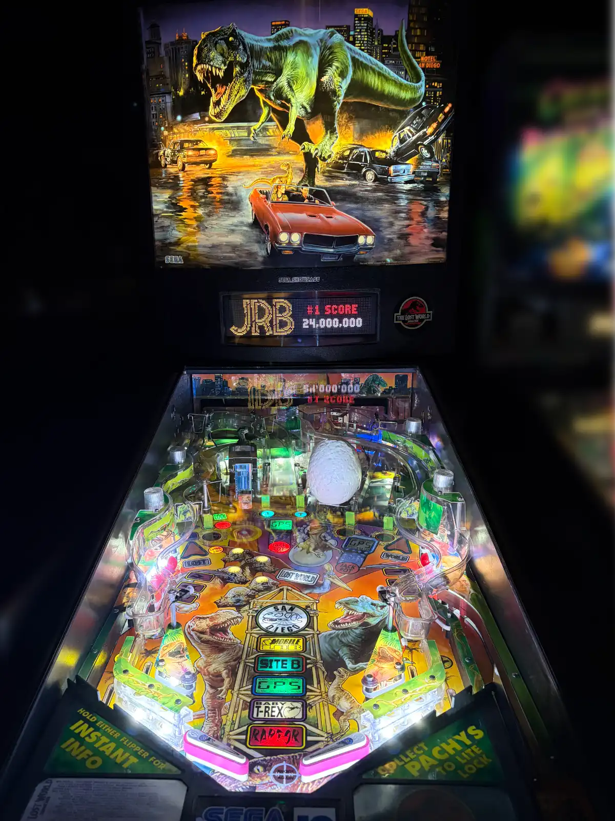 A brightly illuminated pinball machine based on The Lost World: Jurassic Park, featuring a T-Rex on the backglass and complex playfield with lights and dinosaur targets.