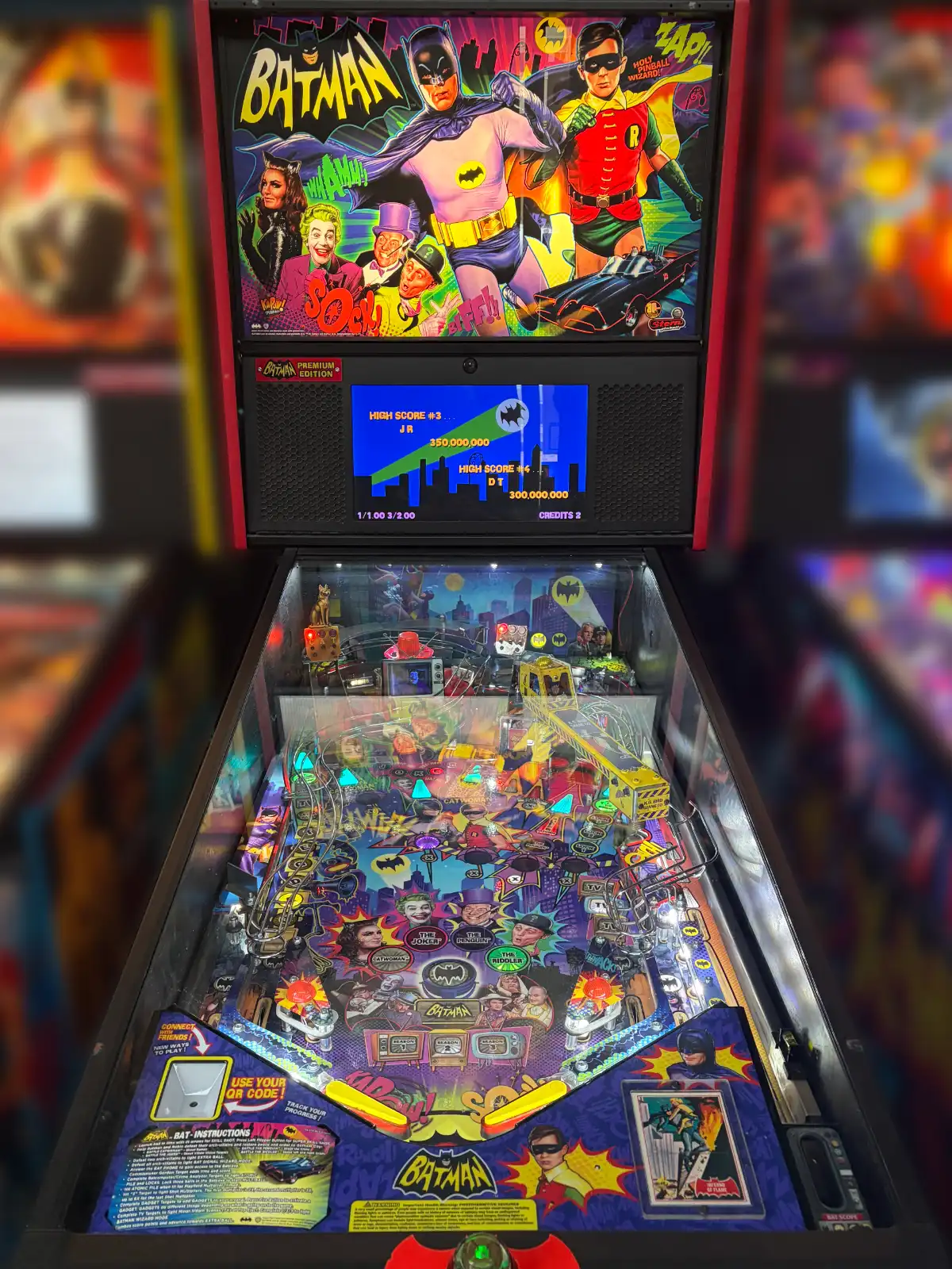A full Batman '66 pinball machine features colorful backboard art of the heroes and villains, a detailed playfield, and a screen showing a 350 million score.