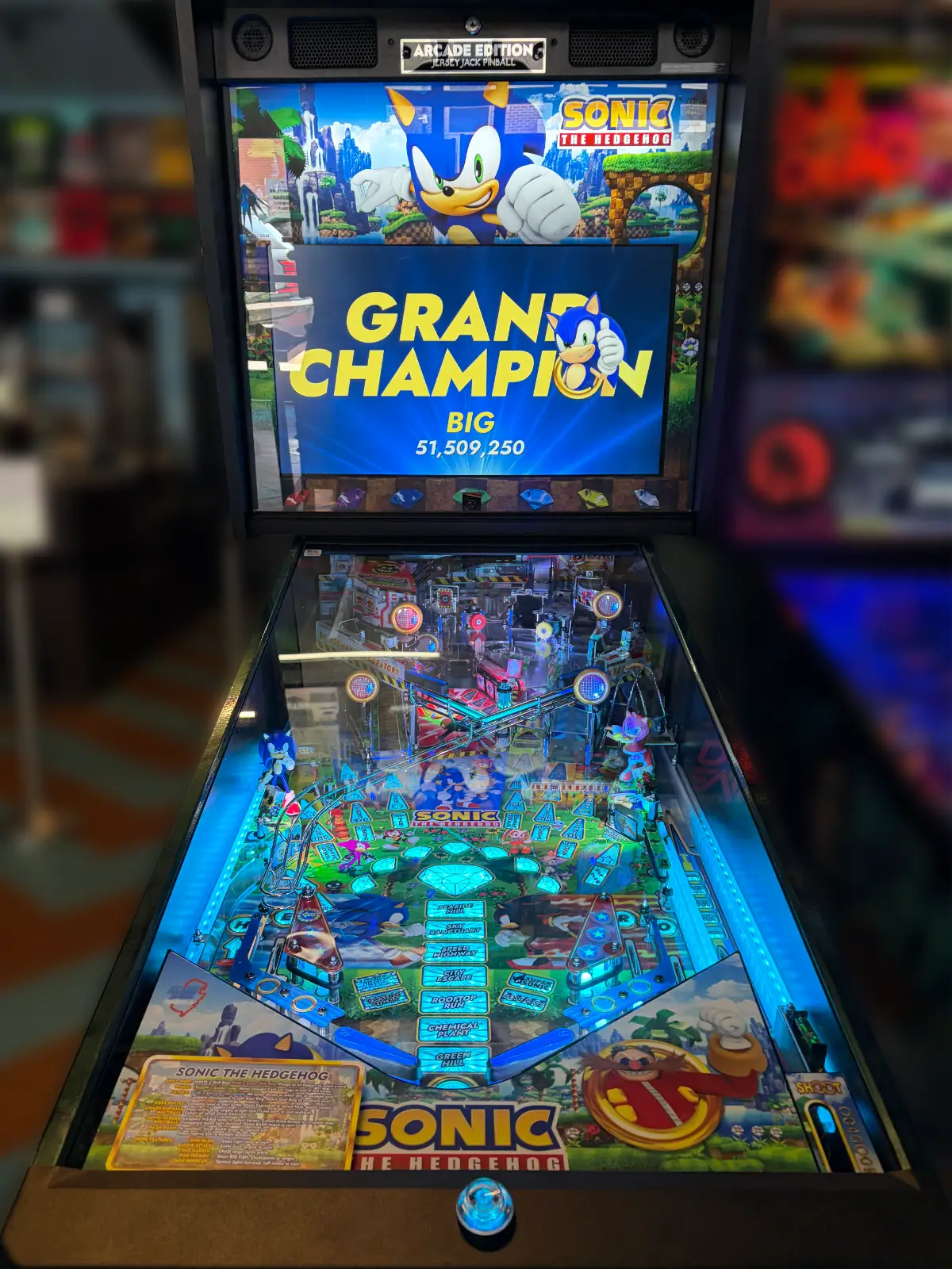 A detailed "Sonic the Hedgehog" pinball machine, illuminated by bright blue LEDs, displays a massive score of 51,509,250 on the "Grand Champion" screen.
