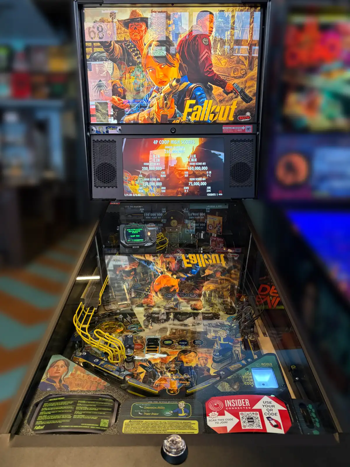 A vertical shot of a modern pinball machine themed after the video game Fallout. It features detailed character art on the backglass and an illuminated playfield.