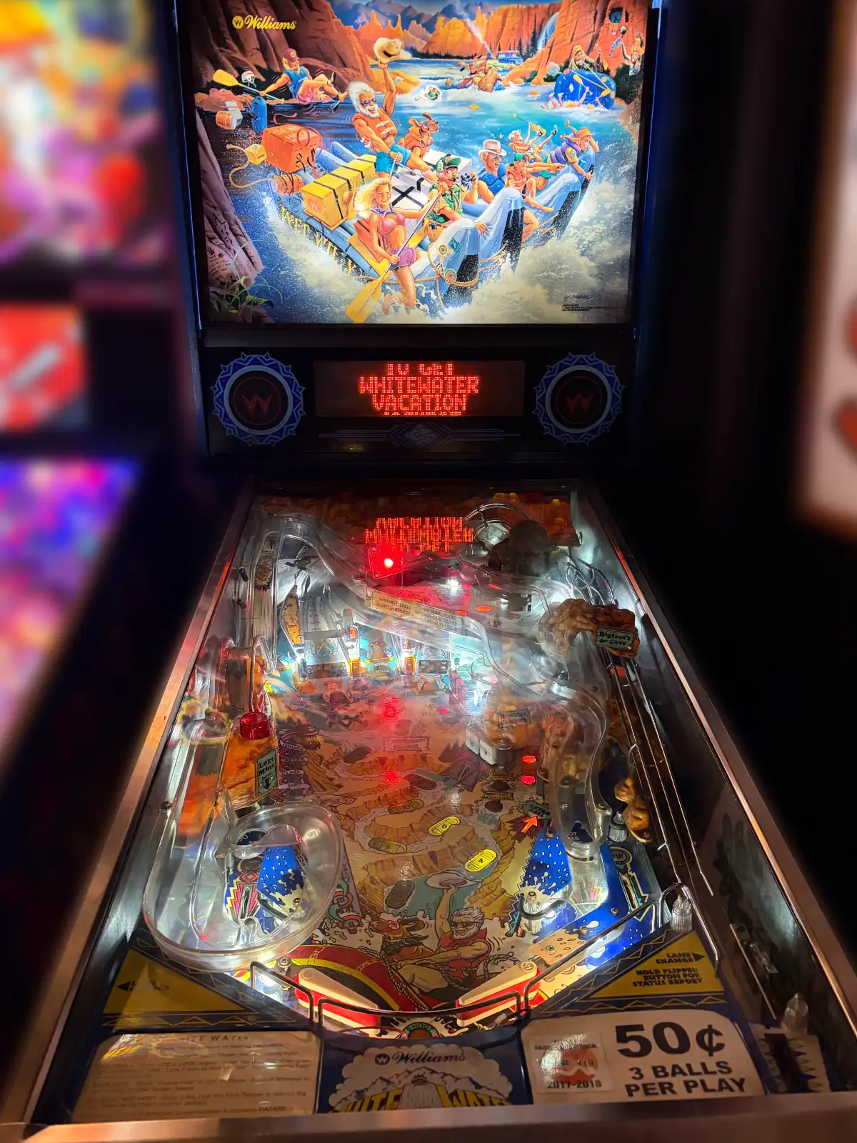 A brightly lit Williams White Water pinball machine. The backglass features cartoon art of a group whitewater rafting. The digital display reads "WHITEWATER VACATION."