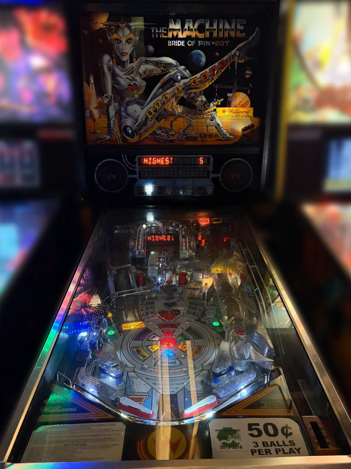 A brightly lit Williams "The Machine: Bride of Pin-Bot" pinball machine. The playfield and backglass, featuring a chrome cyborg, are active in the dark venue.